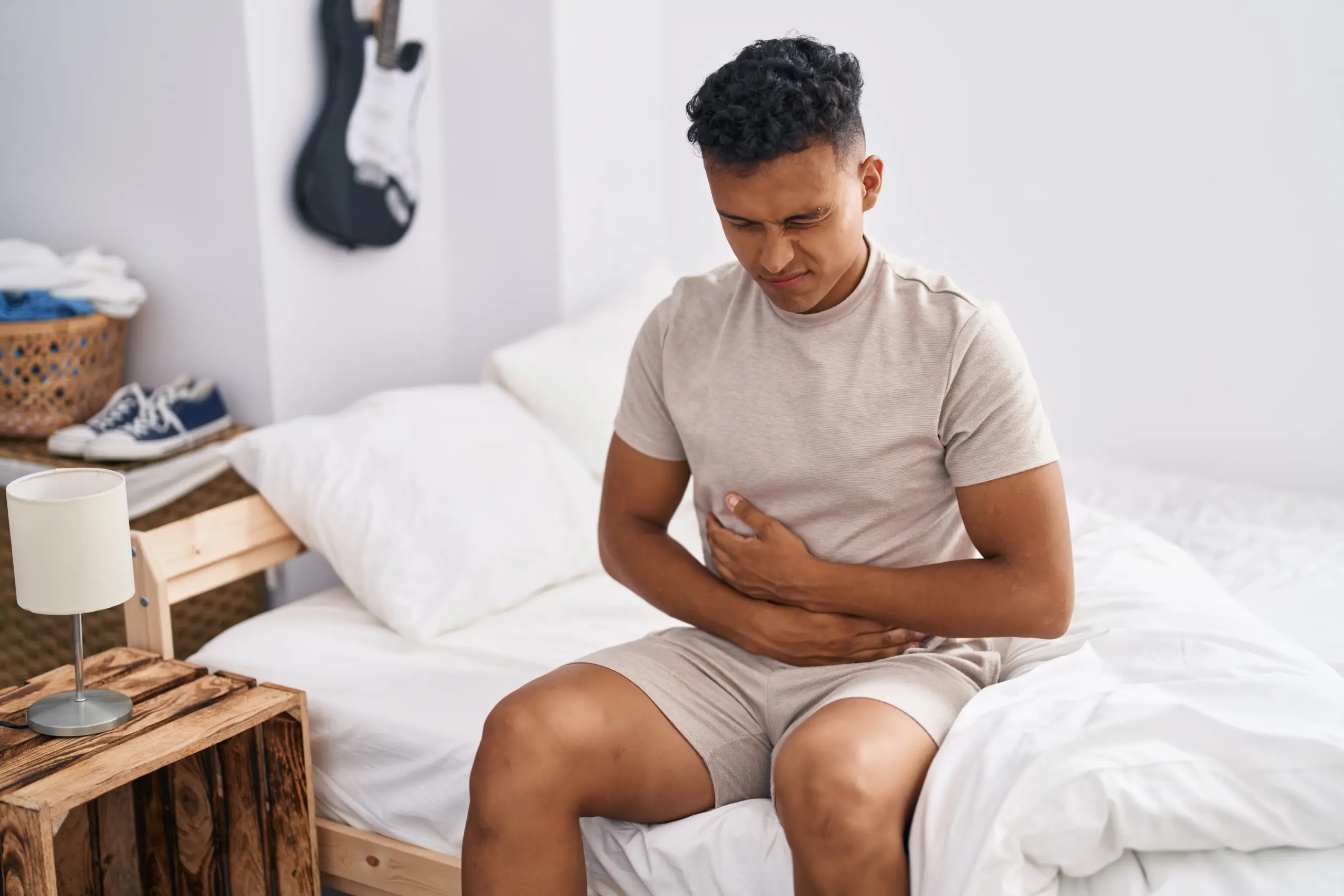 Man sitting on a bed holding his stomach in discomfort from digestive issues