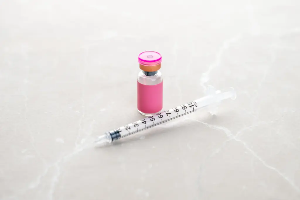 A small glass peptide vial and insulin syringe on a marble surface, illustrating peptide therapy for weight loss support.
