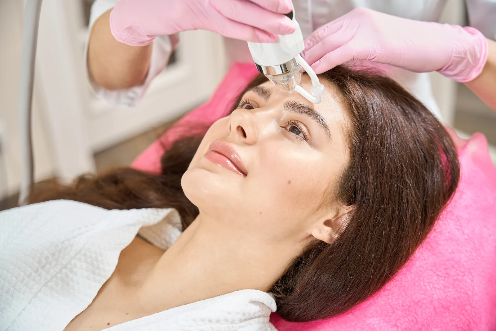 Woman resting on a treatment bed as a gloved clinician applies an RF microneedling handpiece to her forehead in South Tempe, AZ.