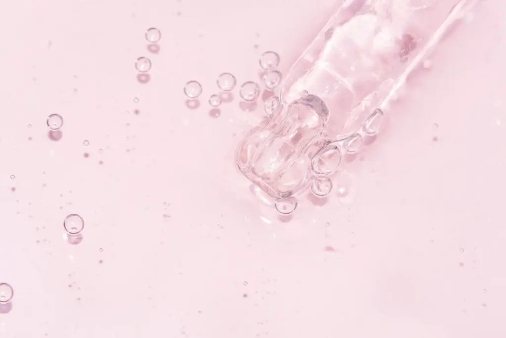 Macro view of a glass dropper releasing clear serum droplets on a soft pink background, like serums used alongside microneedling in Tempe.