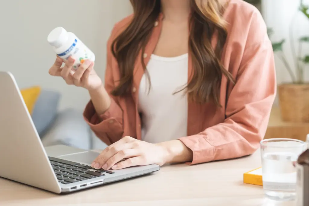 A woman at a laptop reads a supplement bottle label, a reminder to vet online sellers of weight loss medications.