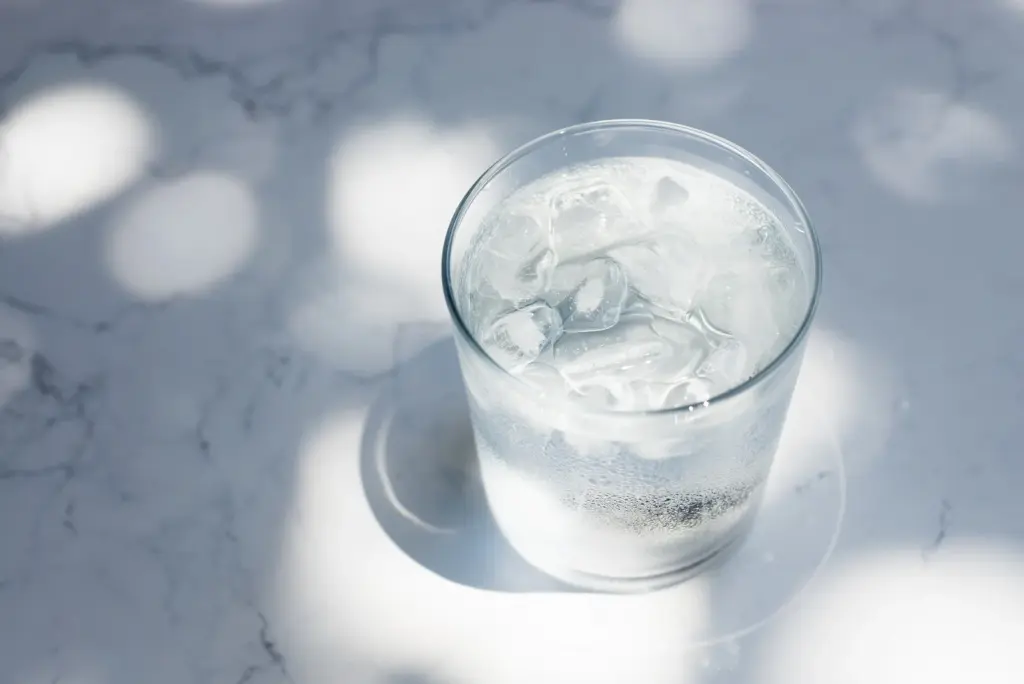 Glass of ice water on a marble table in bright morning sunlight, a simple habit that supports skin hydration in Tempe's dry heat.