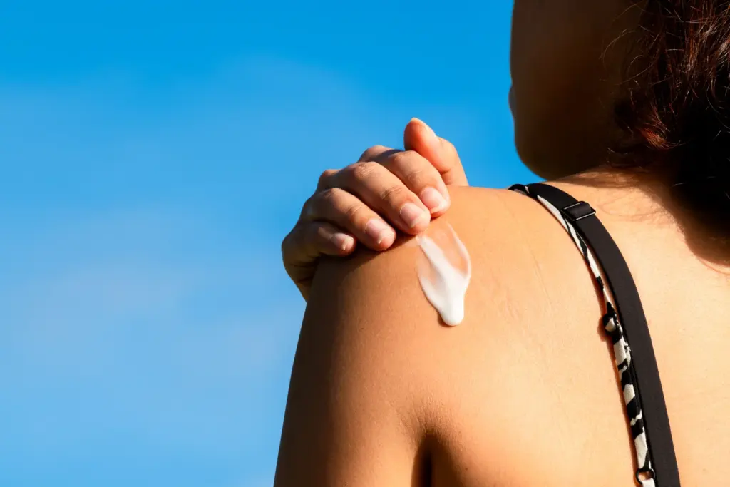Woman applying sunscreen to her sun-exposed shoulder under a bright blue sky, since UV exposure speeds up wrinkles in the Arizona sun.