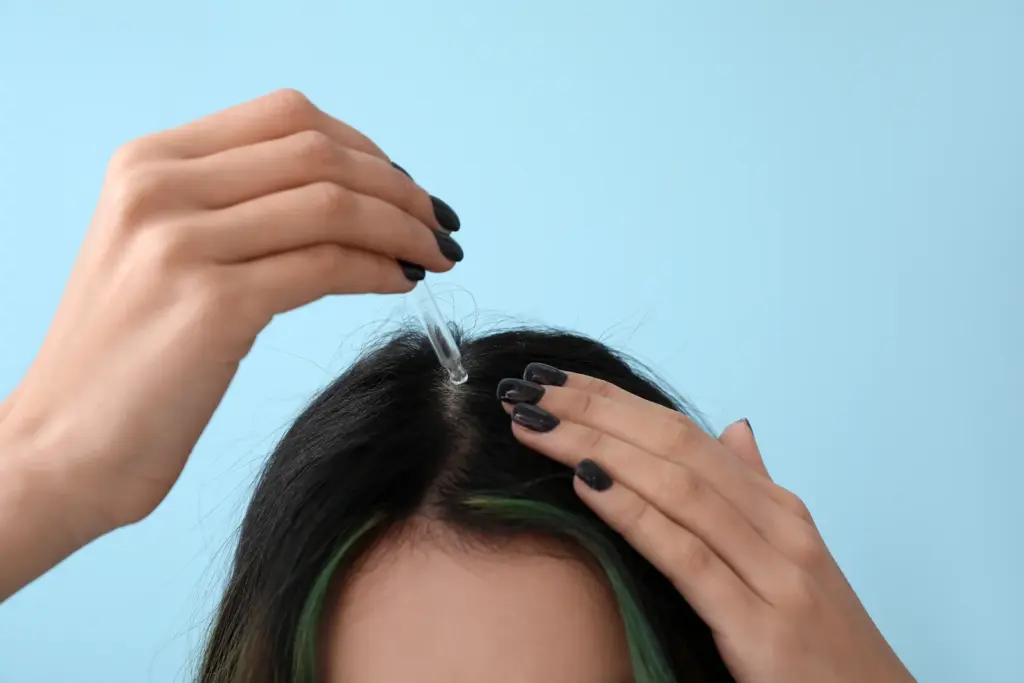 Woman applying a scalp serum with a dropper along her hair part as part of a daily routine to support regrowth at home in Tempe.