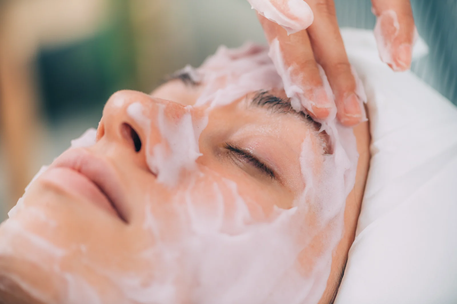 Woman relaxing with eyes closed as a clinician smooths a creamy hydrating mask over her face during a facial in South Tempe, AZ.