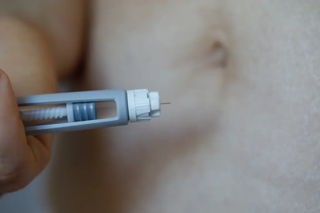 Close view of an unbranded weekly injection pen held near the abdomen, the delivery method used for GLP-1 medications.