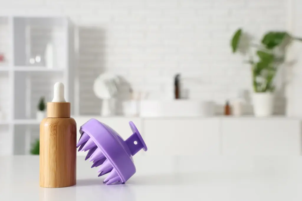 Silicone scalp massager beside a dropper bottle of hair serum on a bright bathroom counter, simple at-home scalp care tools in Tempe.