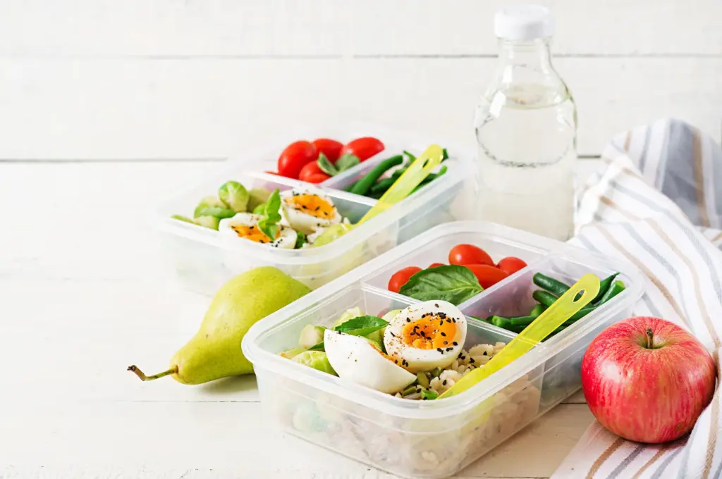 Meal prep containers with eggs, green beans and tomatoes, an example of a whole-food nutrition plan for weight loss.