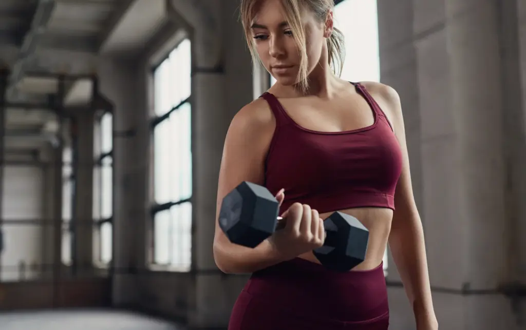 A woman does dumbbell curls in a sunlit gym, strength training that helps preserve muscle during weight loss in Tempe.