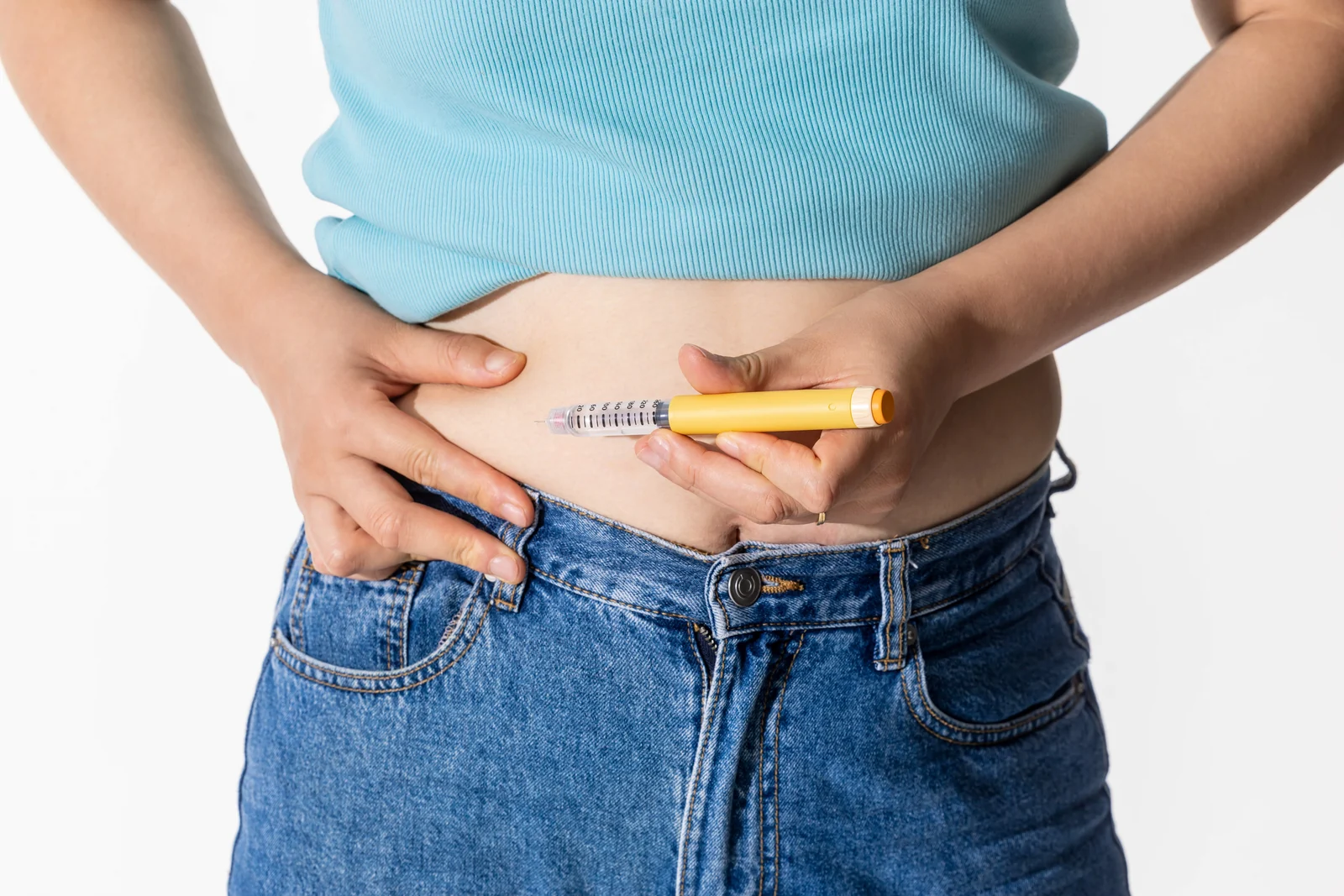 A woman holds a generic injection pen at her abdomen, the weekly delivery method for semaglutide and tirzepatide.
