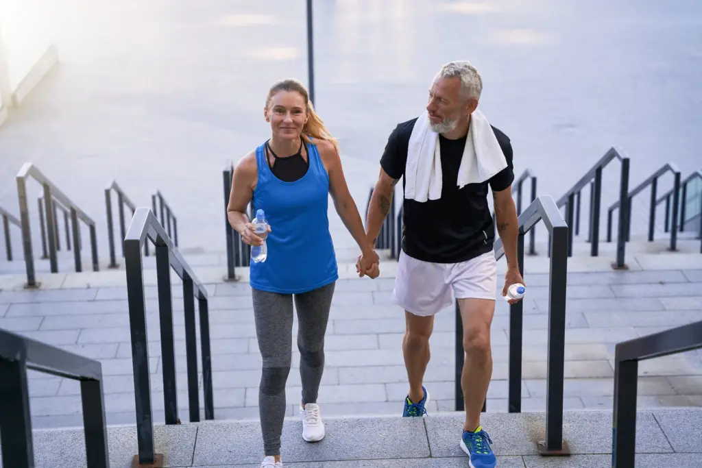 Middle-aged couple in workout clothes holding hands as they climb outdoor steps after exercising together in Tempe.
