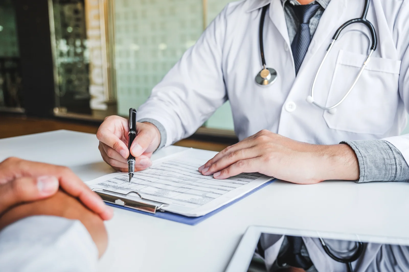 A clinician taking notes on a clipboard across the desk from a male patient during a private men's health consultation in South Tempe, AZ.