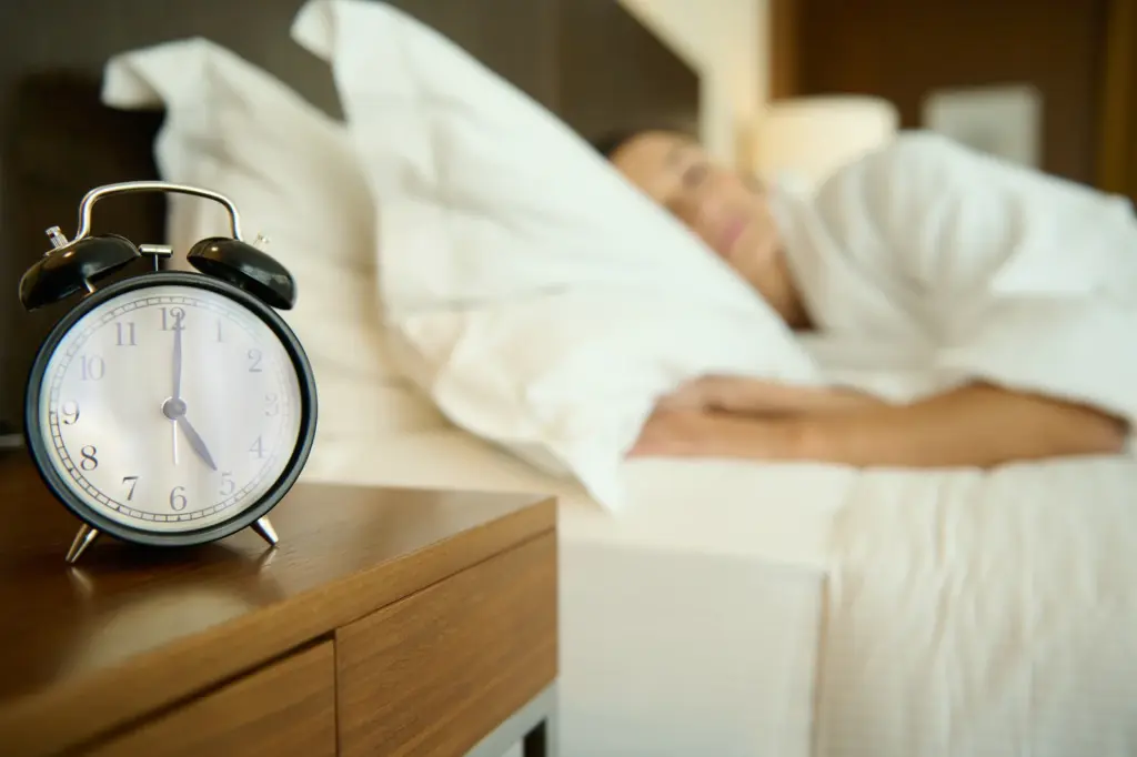 Alarm clock on a nightstand beside a woman sleeping, illustrating the sleep disruption many Tempe women notice in perimenopause.