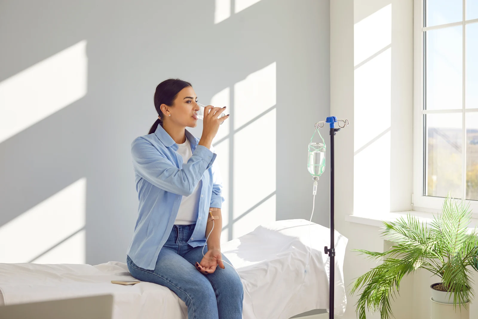 A woman sips water while receiving an IV vitamin drip in a bright treatment room in South Tempe, AZ.