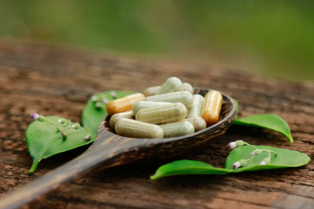 Herbal and vitamin supplement capsules on a wooden spoon with fresh leaves, cofactors that support metabolism.