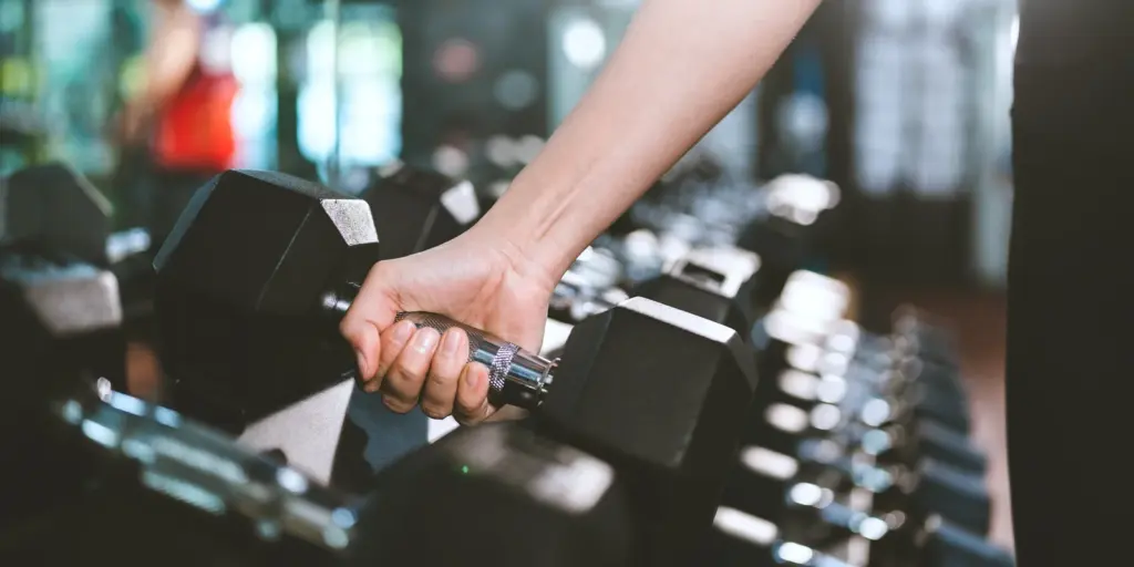Close up of a hand lifting a dumbbell from a gym rack, as strength training builds muscle under loose skin after weight loss in Tempe.