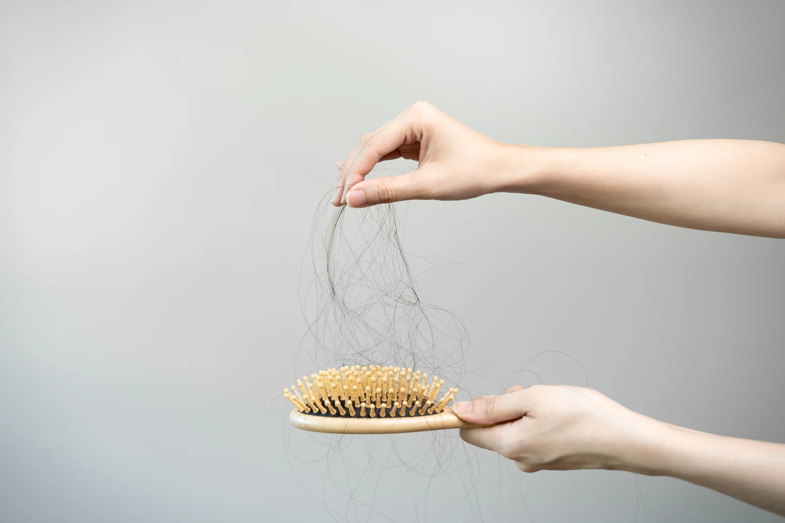 Hands pulling shed strands from a hairbrush, showing the kind of hair shedding some people notice after rapid weight loss in South Tempe, AZ.